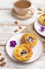 Small cheesecakes with jam and almonds with cup of coffee on a white wooden background and linen