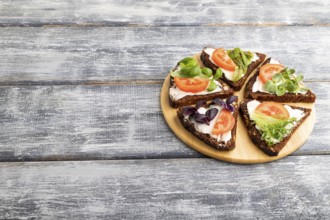 Grain rye bread sandwiches with cream cheese, tomatoes and microgreen on gray wooden background.