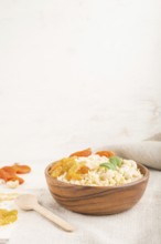 Bulgur porridge with dried apricots, raisins and cashew in wooden bowl on a white wooden background