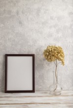 Brown wooden frame mockup with dried hydrangea in glass on gray concrete background. Blank,