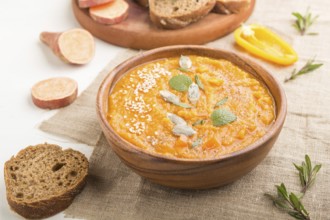 Sweet potato or batata cream soup with sesame seeds in a wooden bowl on a white wooden background