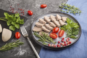 Boiled pork tongue with tomatoes and herbs on a black concrete background and blue linen textile.