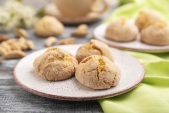 Almond cookies and a cup of coffee on a gray wooden background and green linen textile. Side view,