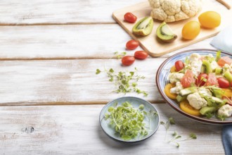 Vegetarian salad of cauliflower cabbage, kiwi, tomatoes, microgreen sprouts on white wooden