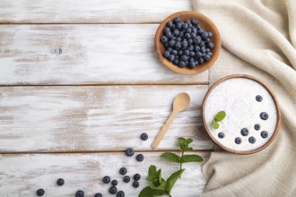 Yogurt with blueberry in wooden bowl on white wooden background and linen textile. top view, flat