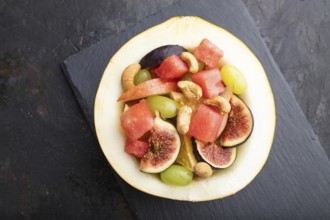 Vegetarian fruit salad of watermelon, grapes, figs, pear, orange, cashew on slate board on a black