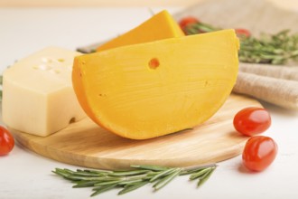 Various types of cheese with rosemary and tomatoes on wooden board on a white wooden background and