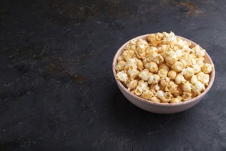 Popcorn with caramel in ceramic bowl on a black concrete background. Side view, copy space