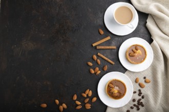 Sweet tartlets with almonds and caramel cream with cup of coffee on a black concrete background and