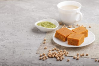 Traditional indian candy burfi in white plate with mint chutney on a gray concrete background. side