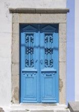 Blue old door with decorative ironwork in a stone frame in front of a white Mediterranean-style