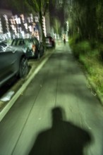 Pedestrian path in the evening, dark, little lighting from street lamps, shadow of a man, following