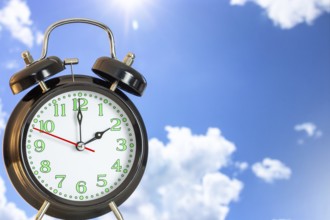 Symbolic image of the time change to summer time: close-up of an alarm clock in front of a blue sky