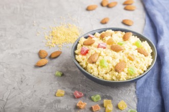 Millet porridge with candied fruits and almonds in blue ceramic bowl on a gray concrete background