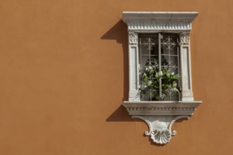 Small house altar with lattice and flowers on an orange-coloured house facade, Venice, Italy,