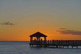 Silhouette of a jetty against the orange coloured sky at dusk without visible people, Dominicus