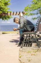 Man sitting on a bench checking his phone, young man checking his cell phone sitting on a bench