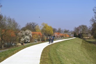 Three people walking and cycling along a path past blossoming trees, Elbe dyke, Damnatz, Wendland,