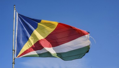 The flag of Seychelles, fluttering in the wind, isolated against a blue sky