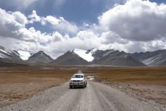 Off-road vehicle on a gravel track, glaciated and snow-covered peaks, Ak Shyrak Mountains, near