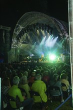 Open-air concert at night with illuminated stage and a large crowd and green lights, Klostersommer,