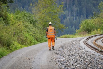 Construction worker in orange protective clothing walks along a gravel path, track construction,