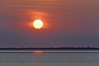 Sunset over the North Sea at low tide, the outline of the island of Juist on the horizon,