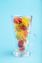 Various fruit jelly candies in drinking glass on blue pastel background. side view, close up