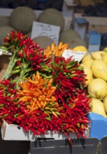 Different coloured peppers on a market stall next to other fruits