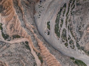 Off-road vehicle on a track in a riverbed, landscape of eroded hills, top-down, badlands, aerial