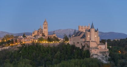 A majestic castle on a hill at dusk with illuminated buildings and a mountain backdrop, Cathedral,