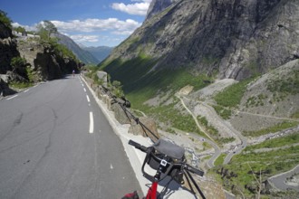 A mountain road winding through the landscape with a bicycle in the foreground, Trollstigen,