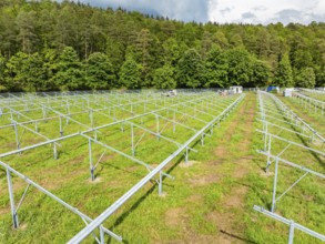 Metal frame of a solar park under construction, located at the edge of a forest under a cloudy sky,