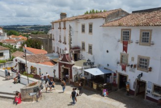 People walking through a cobbled historic city centre with white buildings and red roofs, view from