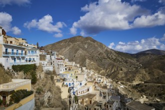 Village on a mountainside under a bright blue sky with clouds, Colourful mountain village, Morning