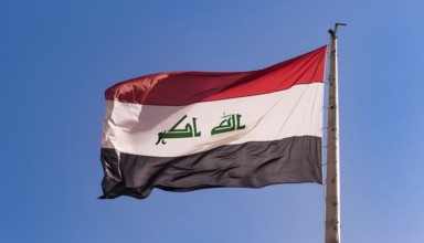 The flag of Iraq flutters in the wind, isolated against a blue sky