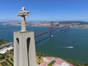 Statue with outstretched arms on a viewpoint next to a red bridge and an extensive cityscape in the