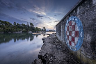 Graffiti on a stone wall overlooking the sea with a boat at sunrise, Korcula, Croatia, Europe