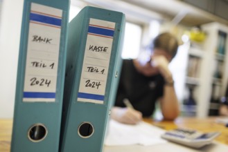 Symbolic photo: A woman sits at a desk in an office with a calculator and file folders and does