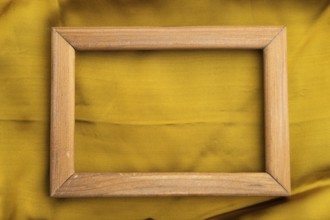 Wooden frame on smooth yellow silk tissue. Top view, flat lay, natural textile background and