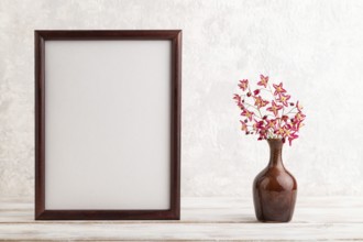 Wooden frame with purple barrenwort flowers in ceramic vase on gray concrete background. side view,