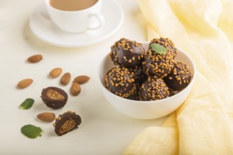 Chocolate caramel ball candies with almonds and a cup of coffee on a white wooden background and