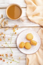 Orange macarons or macaroons cakes with cup of apricot juice on a white wooden background and