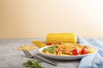 Corn noodles with tomato sauce and arugula on a gray and orange background and blue textile. Side