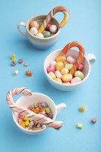 Heap of multicolored caramel candies in cups on blue pastel background. close up, side view