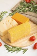 Various types of cheese with rosemary and tomatoes on wooden board on a white wooden background and