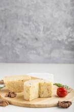 Cheddar and various types of cheese with rosemary and tomatoes on wooden board on a gray and white