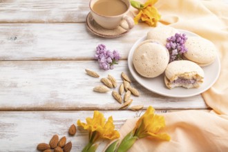 Meringues cakes with cup of coffee on a white wooden background and orange linen textile. Side