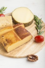 Smoked cheese and various types of cheese with rosemary and tomatoes on wooden board on a white