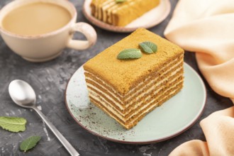 Homemade honey cake with milk cream and mint with cup of coffee on a black concrete background and